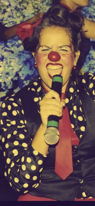 Palhaça Dita com nariz vermelho ao microfone